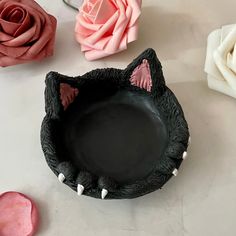 there is a black cat shaped bowl on the table next to some pink and white roses