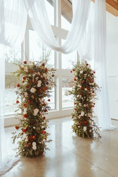 two tall floral arrangements in front of a window