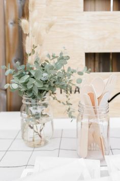 two mason jars filled with utensils sitting on top of a white table cloth