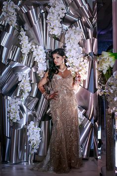 a woman standing in front of a large metal structure with flowers on the side and an umbrella behind her