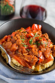 a bowl filled with meat and vegetables on top of mashed potatoes next to a glass of wine