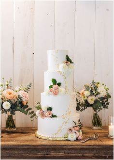 a three tiered wedding cake sitting on top of a table next to vases filled with flowers