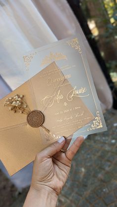 a person holding up a gold and white wedding card