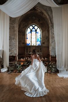 a woman in a white wedding dress standing on a wooden floor next to a stained glass window