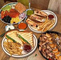 three plates with different types of food on them sitting on a wooden table next to bowls of sauces and condiments