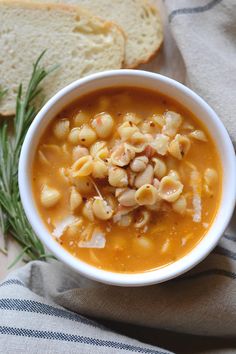 a white bowl filled with pasta soup next to a slice of bread on top of a blue and white towel