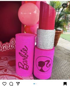 two pink lipstick tubes with the word barbie written on them and balloons in the background