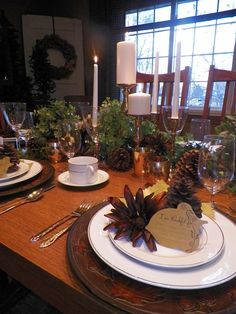 a table set with place settings and pine cones