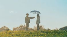 two people standing on top of a hill holding an umbrella