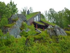 a house with a green roof on top of a hill covered in grass and rocks