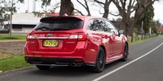 a red subarunt is parked on the side of the road in front of some trees