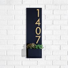 a house number sign mounted to the side of a white brick wall with a succulent plant in it