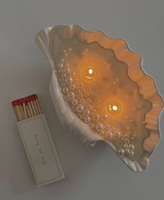 two candles are lit in a shell shaped bowl next to matchesticks on a white surface