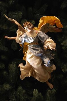 an angel figurine is flying through the air above pine branches and evergreens