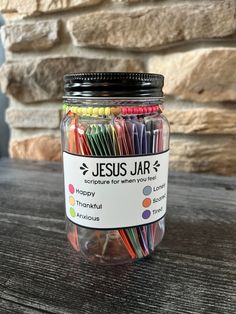 a jar filled with lots of colored straws on top of a wooden table next to a stone wall