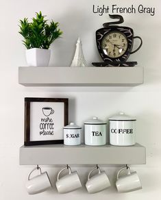 there are coffee mugs and tea cups on the shelf next to each other, along with a clock