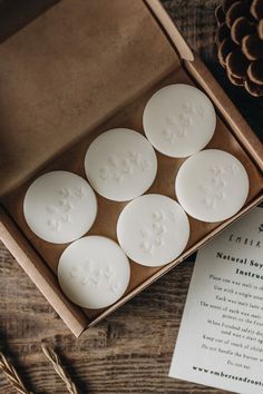 four white soaps in a box on a table next to pine cones and paper