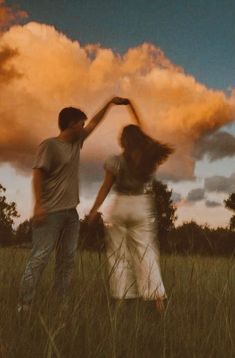 two people standing in the grass with their arms around each other and one person reaching up into the sky