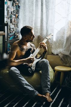 a man sitting on a couch holding an electric guitar in his hand and looking out the window