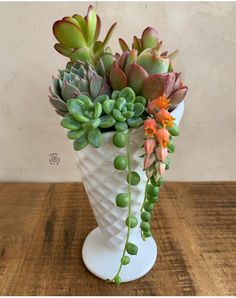 a white vase filled with succulents on top of a wooden table