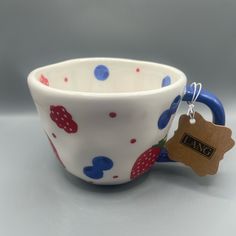 a white cup with red, blue and green polka dots on it has a tag hanging from the handle