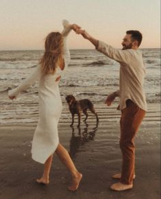 a man and woman dancing on the beach with their dog