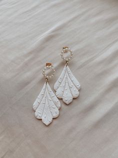 two pairs of white earrings with pearls hanging from them on top of a beige sheet