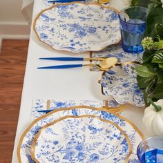 the table is set with blue and white plates, gold trimmings and flowers