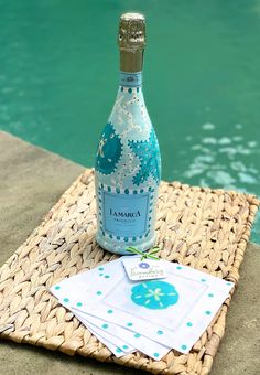 a bottle of wine sitting on top of a table next to a swimming pool and napkins