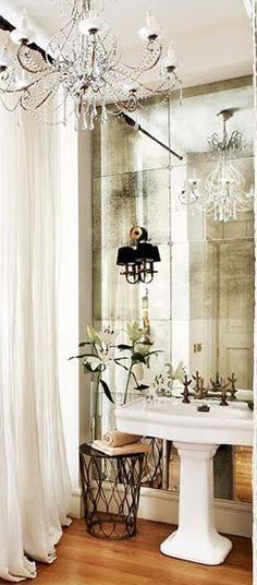 a white pedestal sink sitting in front of a mirror next to a chandelier