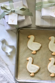 decorated cookies in the shape of ducks are on a baking sheet next to wrapped presents