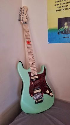 a green electric guitar sitting on top of a bed next to a wall hanging poster