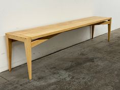 a wooden bench sitting on top of a cement floor next to a white brick wall