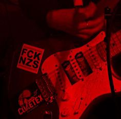 a person holding an electric guitar with red light in the background and stickers on it