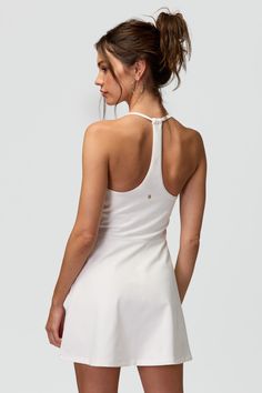 a woman wearing a white tennis dress with her back turned to the camera and looking down