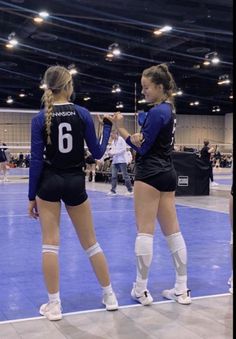 two female volleyball players standing on a court with their hands in each other's pockets