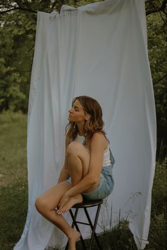 a woman sitting on top of a chair next to a white curtain