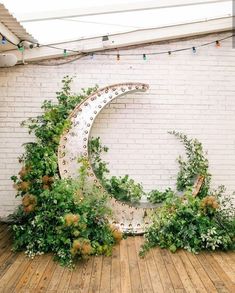 an artistic sculpture made out of metal and greenery sits on a wooden floor in front of a white brick wall