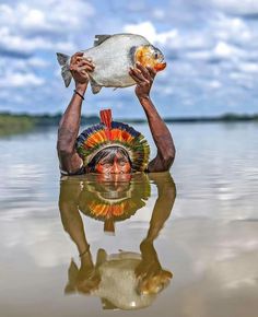 a man holding up a fish over his head in the middle of a body of water