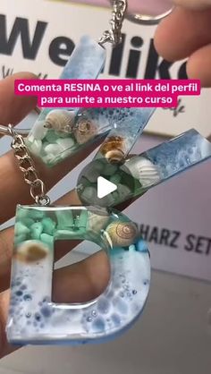 a person holding up a glass letter keychain with seashells on it