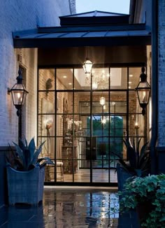 an entrance to a building with glass doors and potted plants on the side walk