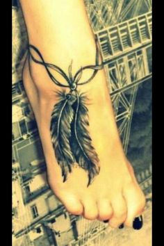 a woman's foot with a tattoo on it and a feather hanging from the ankle