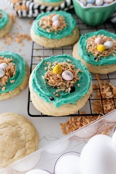 some cookies are decorated with blue icing and candy eggs on a cooling rack in front of other cookies