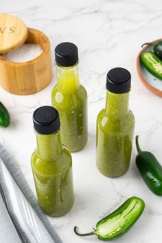 three bottles filled with pickles sitting on top of a counter next to silverware