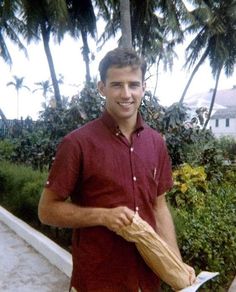 a man in a red shirt is holding an umbrella and smiling at the camera with palm trees behind him