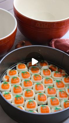 an orange and white cake in a pan on a table with two bowls next to it