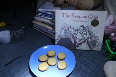 some cookies are on a blue plate next to a teddy bear and a copy of the keeping quilt