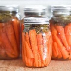 four jars filled with carrots sitting on top of a wooden table