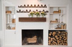 a fireplace with white brick and wooden shelves filled with books, logs and flowers on the mantel