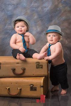 two baby boys sitting on top of suitcases with hats and ties around their necks